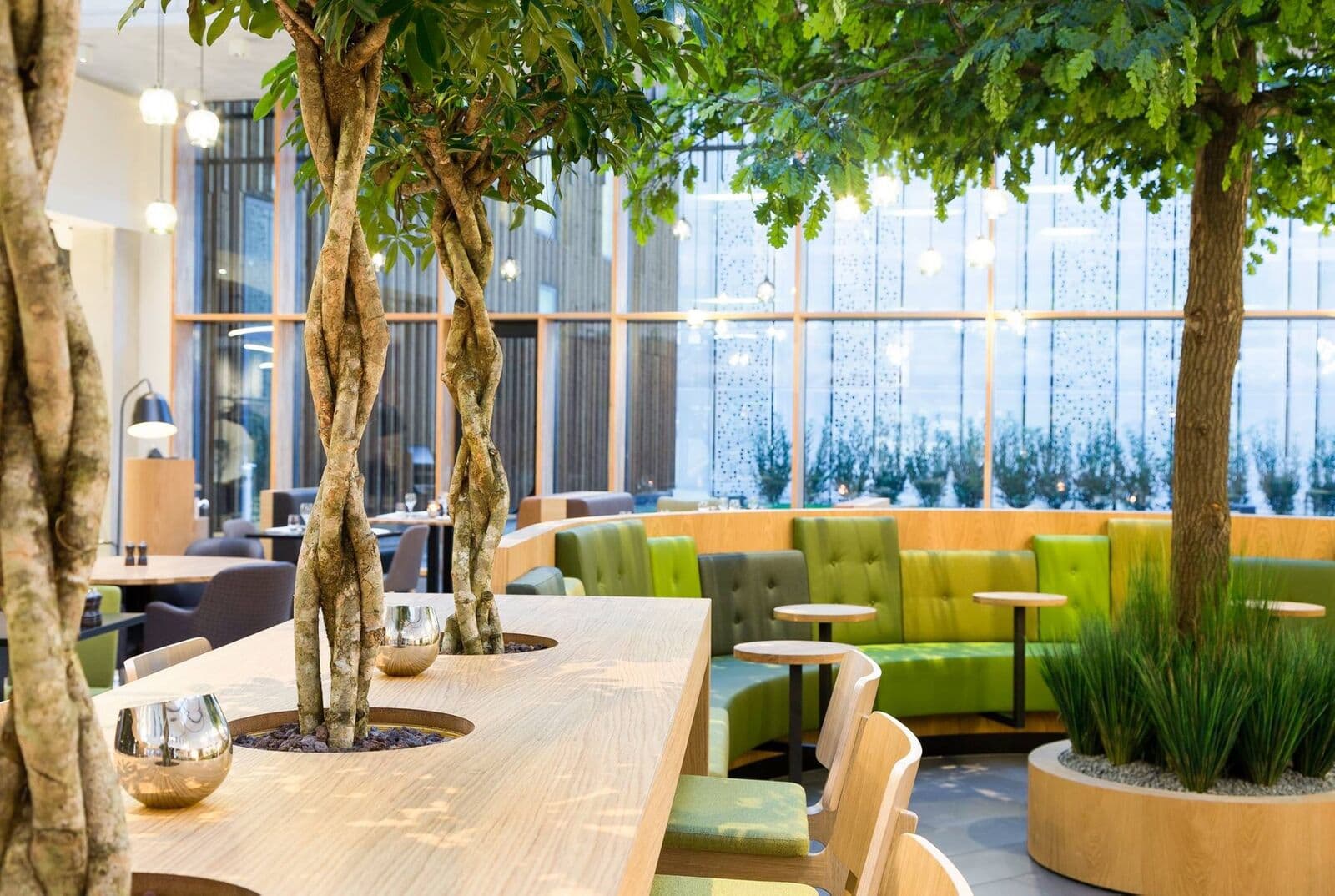 Kunstbomen met gevlochten stammen door een lange tafel in Novotel Schiphol